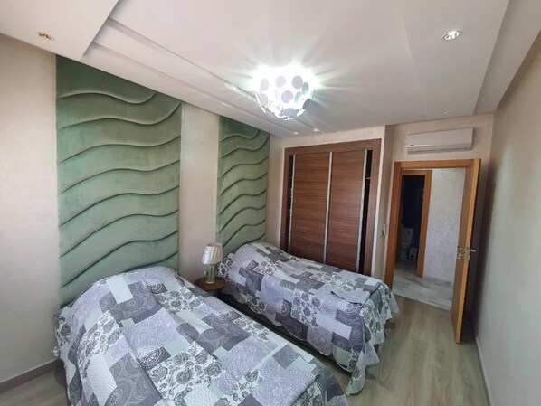 A bedroom with two beds, a nightstand, a wall-mounted light fixture, and a wardrobe.