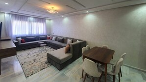 Ein modernes Wohnzimmer mit einer Eckcouch, einem Esstisch mit Stühlen, einem Teppich und einer Deckenleuchte.