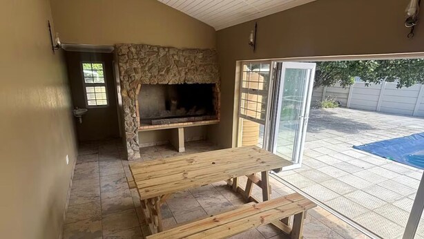 Un área de patio con chimenea de piedra, bancos de madera y una puerta corrediza de vidrio que da a un jard ín trasero.