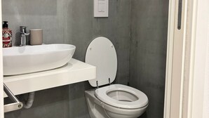 A modern bathroom with a white toilet, a white sink, and a shower area. - At Casuzza di Giù Giù: Experience your stay in the historic center of Agrigento! (Agrigento)