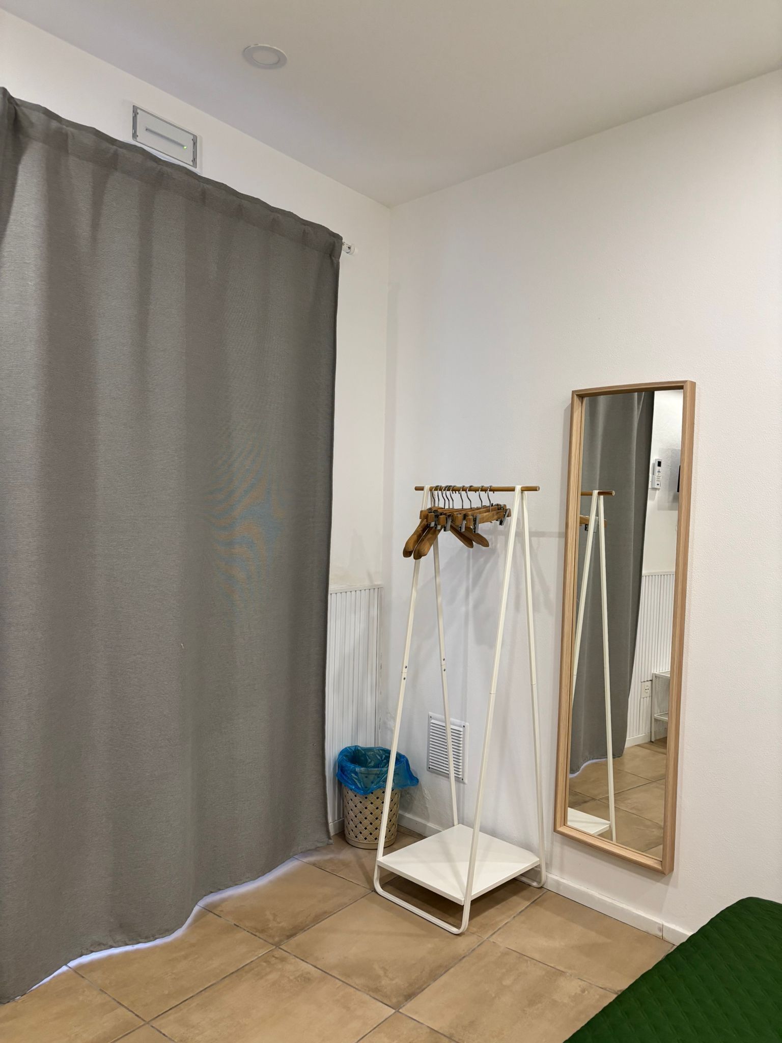 A room with a grey curtain, a white shelf unit, a mirror, and a radiator.