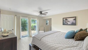 Ein Schlafzimmer mit Bett, Deckenventilator, Schreibtisch und Blick ins Freie.
