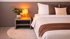 Une chambre à coucher bien rangée, avec un lit, des oreillers, une table de chevet avec une lampe et une plante en pot.