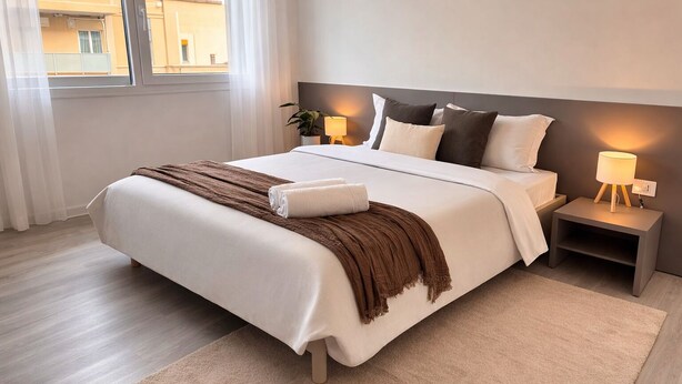 Un lit bien fait, avec une couverture marron, une lampe de chevet et une table de nuit.