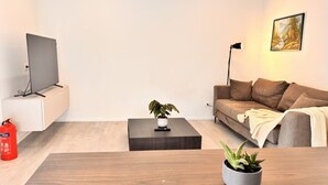 Un salon moderne avec un téléviseur à écran plat, un canapé, une table basse, une plante en pot et un extincteur.