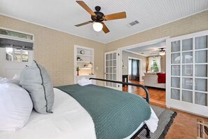 A bedroom with a bed, pillows, a ceiling fan, a nightstand, a window, and a door leading to a living area. - Park Free Walk to SoCo Ride to DT/UT/COTA (Austin)