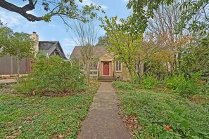 A pathway leading to a house with a red door, surrounded by greenery and a wooden fence. - Park Free Walk to SoCo Ride to DT/UT/COTA (Austin)