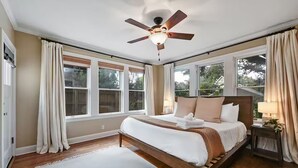 A bedroom with a bed, a ceiling fan, large windows, and a view of trees. - Park Free  Walk to SoCo  Ride to DT/UT/COTA (Austin)