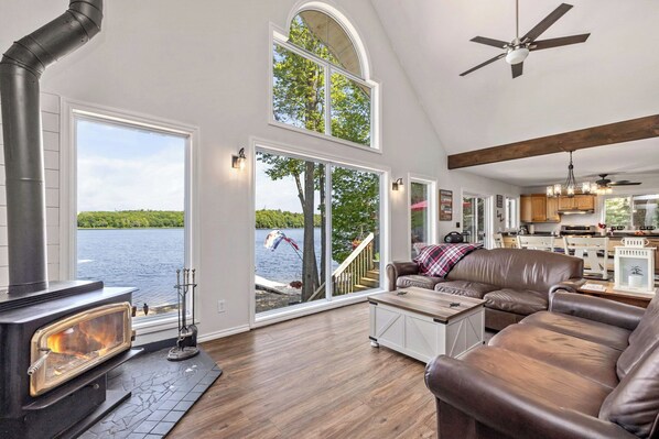 A spacious living room with a fireplace, large windows, a loft bedroom, and a kitchen.