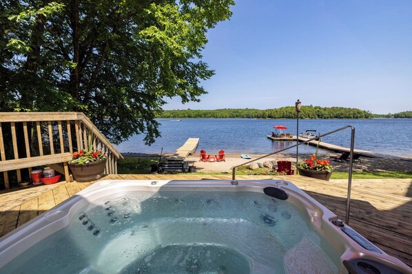 Eine Holzterrasse mit Whirlpool, Sitzgelegenheit und Seeblick.