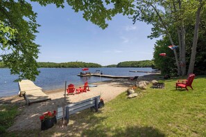 A lakeside setting with a dock, red Adirondack chairs, a bench, and a fire pit.