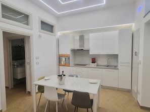 A modern kitchen with white cabinetry, a dining table with chairs, and a built-in oven. - Suite with private relaxation area, mood lighting, and music – near Pompeii. (Sant'Antonio Abate)