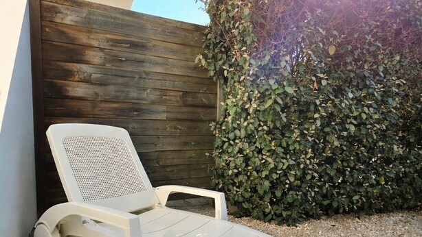 A white lounge chair with a perforated backrest and armrests, positioned on a stone patio adjacent to a wooden fence and a hedge. - Studio St Gilles X Vie between beach, town and port. (Saint-Gilles-Croix-de-Vie)