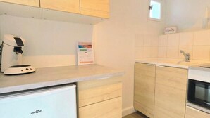 A compact kitchen with light wood cabinets, a built-in oven, and a small refrigerator. - Studio St Gilles X Vie between beach, town and port. (Saint-Gilles-Croix-de-Vie)