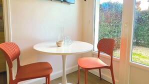A room with a round white table, two red chairs, a flat-screen TV mounted on the wall, and a sliding glass door leading to an outdoor area. - Studio St Gilles X Vie between beach, town and port. (Saint-Gilles-Croix-de-Vie)
