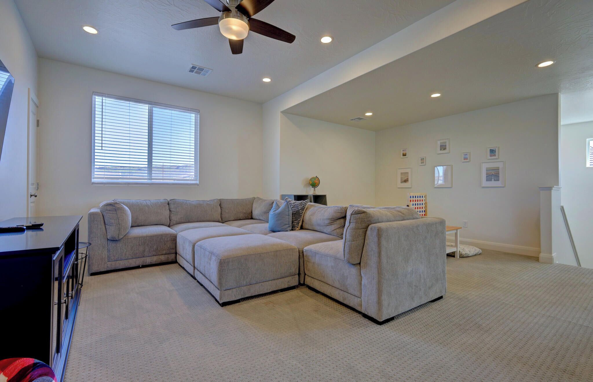 A living room with a sectional sofa, ceiling fan, and recessed lighting.