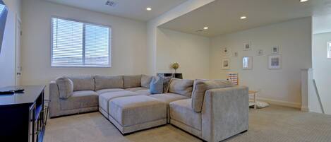A living room with a sectional sofa, ceiling fan, and recessed lighting.