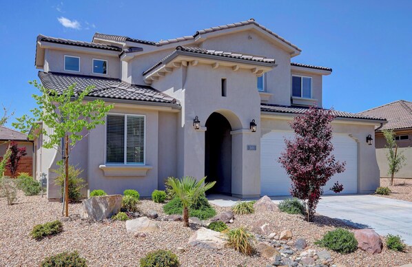 A two-story house with a tiled roof, a central entrance with an archway, and a garage door.