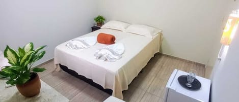 A small, clean room with a bed, a bedside table, a potted plant, and an air conditioning unit.