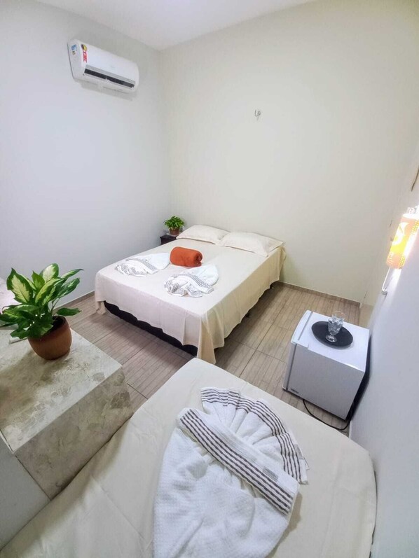 A small, clean room with a bed, a bedside table, a potted plant, and an air conditioning unit.