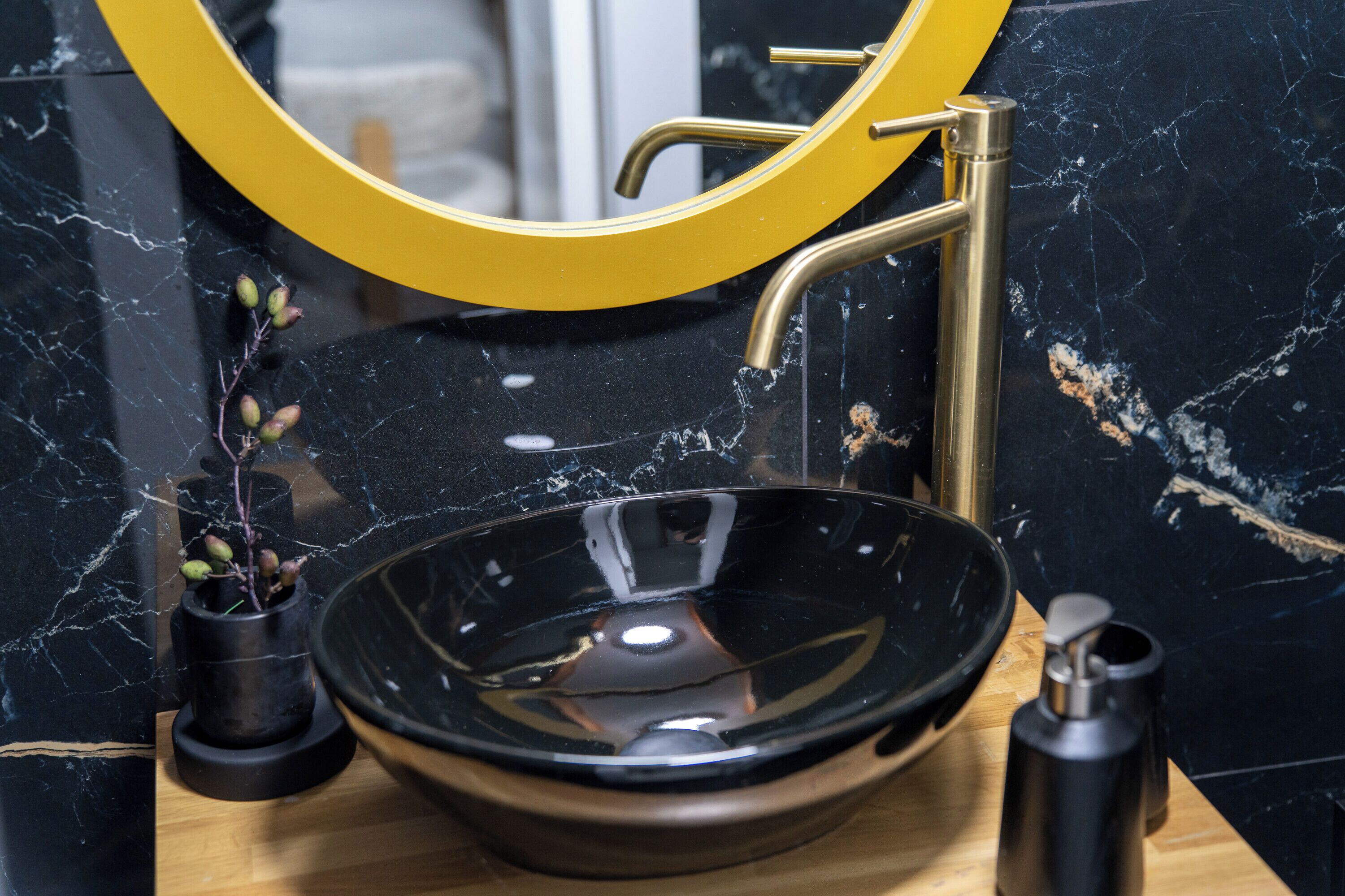 A bathroom with a black marble sink, gold faucet, and a yellow-framed mirror.
