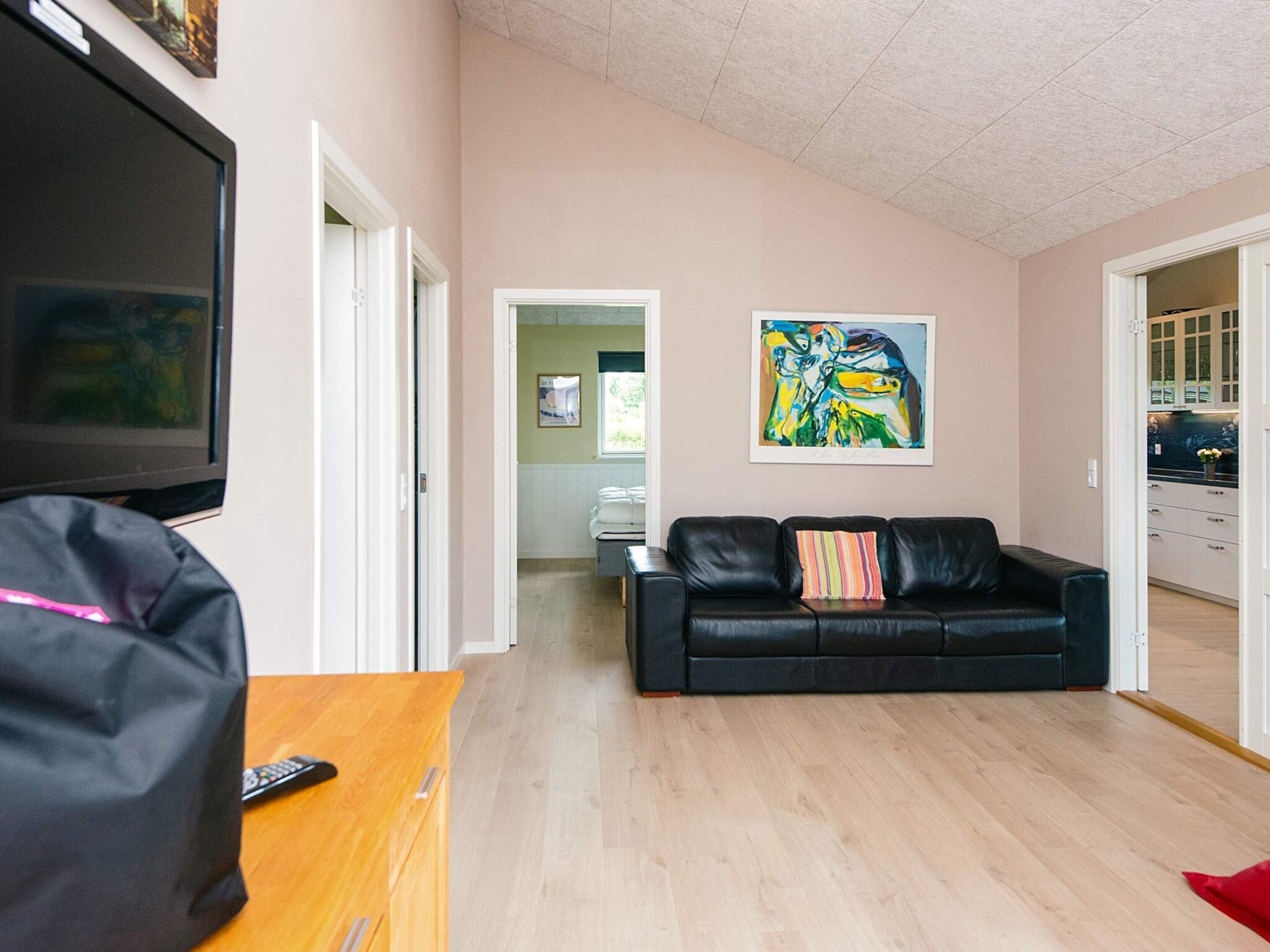 A living room with a black leather sofa, a television, and a painting on the wall.