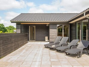 Una casa moderna con techo de tejas, un porche cubierto con sillones de descanso y una cerca de madera.