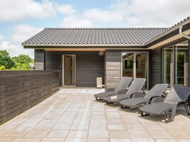 Una casa moderna con techo de tejas, un porche cubierto con sillones de descanso y una cerca de madera.