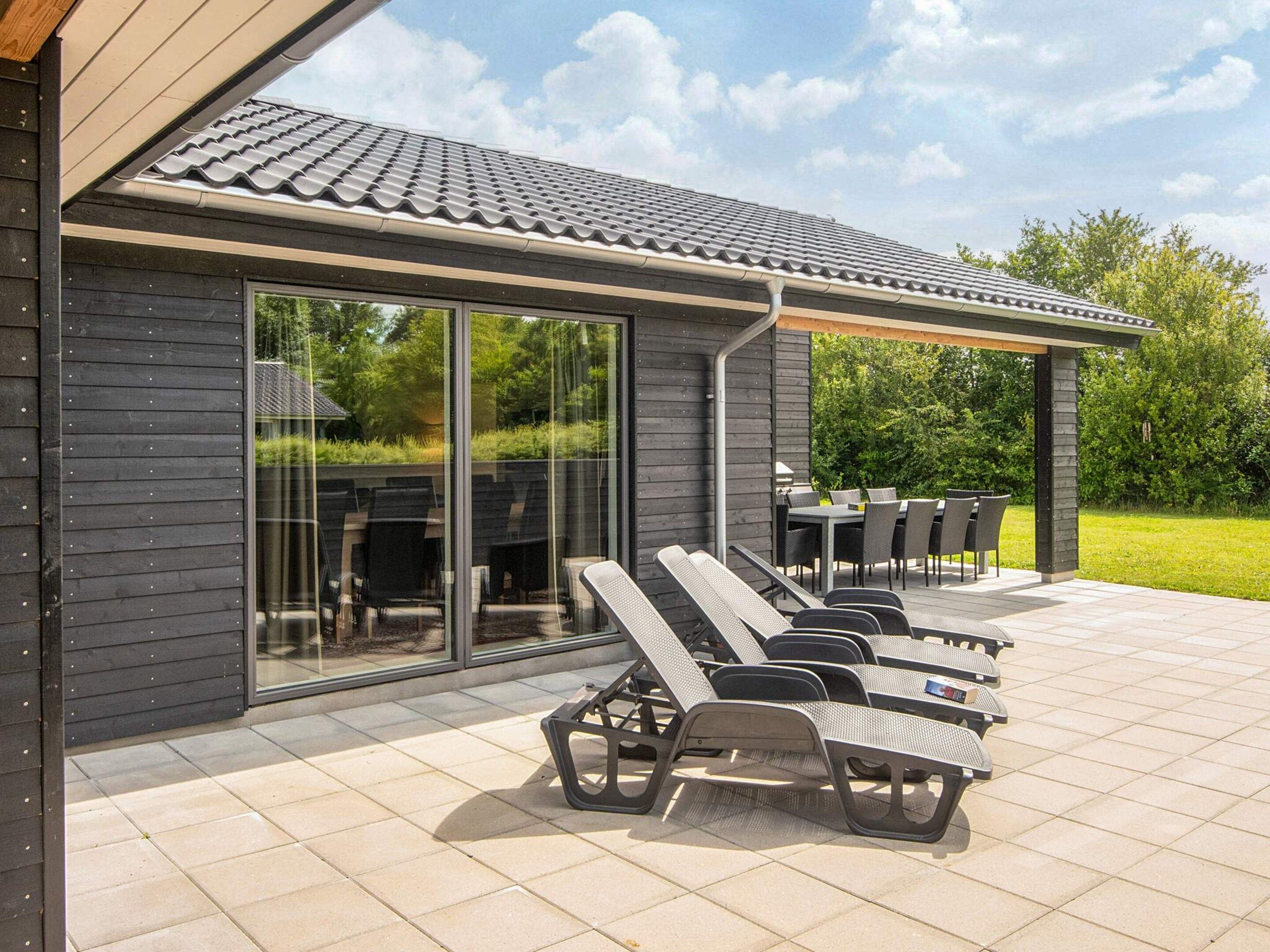 A modern outdoor patio with a covered seating area, a dining table, and a glass door leading to a garden.