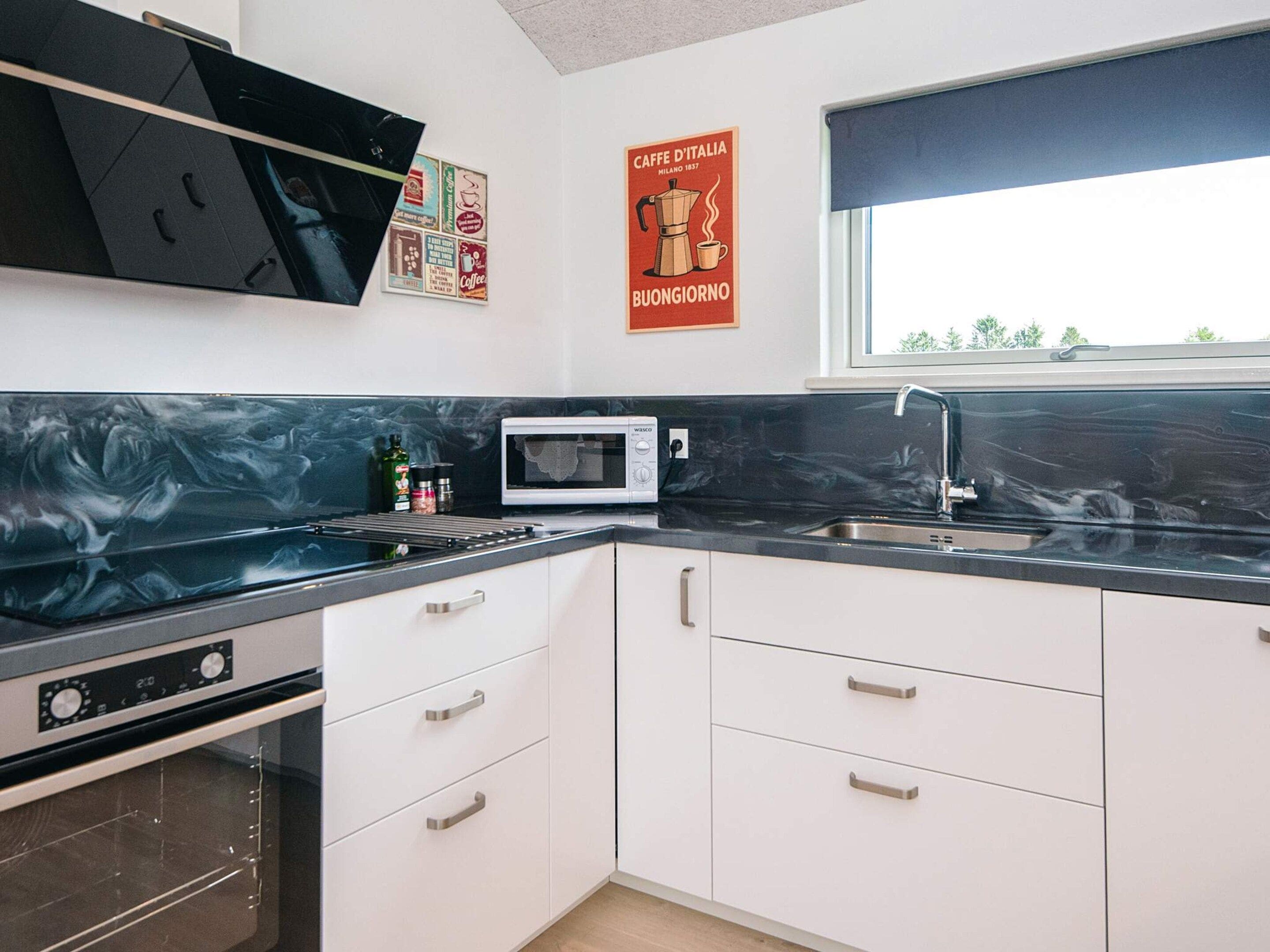 A modern kitchen with white cabinets, a black countertop, a microwave, and a stainless steel sink.