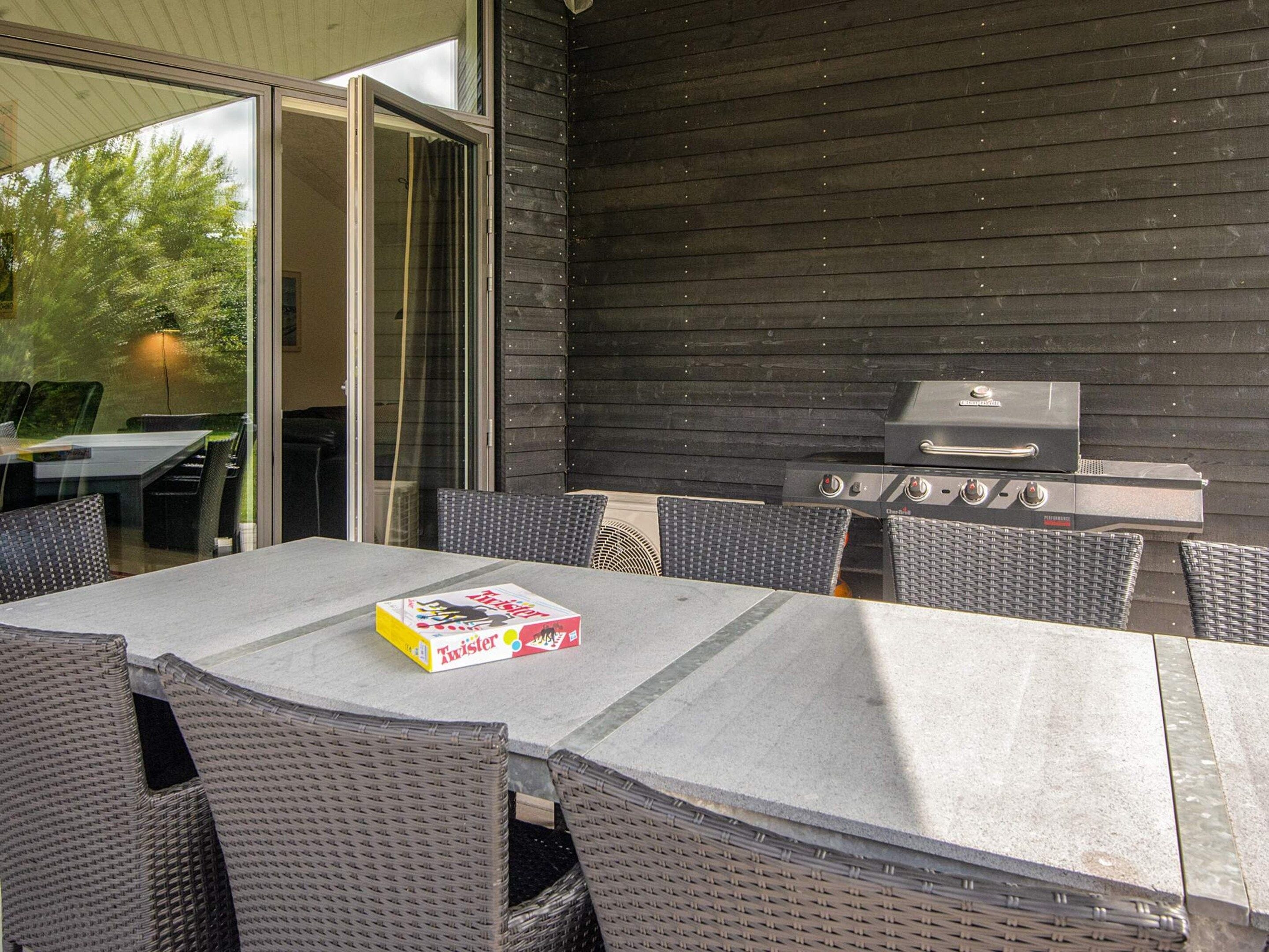 En udendørs terrasse med bord og stole, grill og en skydedør.