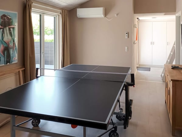 Una mesa de ping pong en una habitación con puerta corredera de vidrio, un aire acondicionado blanco y un armario de madera.