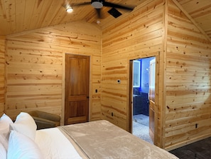 A wooden cabin interior with a bed, a ceiling fan, and a bathroom visible through an open door. - Luxury Giraffe experience in our luxurious 4 bedroom solar powered Giraffe House (Lometa)