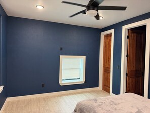 Ein Schlafzimmer mit Deckenventilator, einem Fenster mit Jalousien und einer Tür.