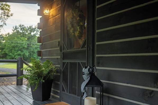 A wooden cabin with a porch, a lantern, and a potted plant.