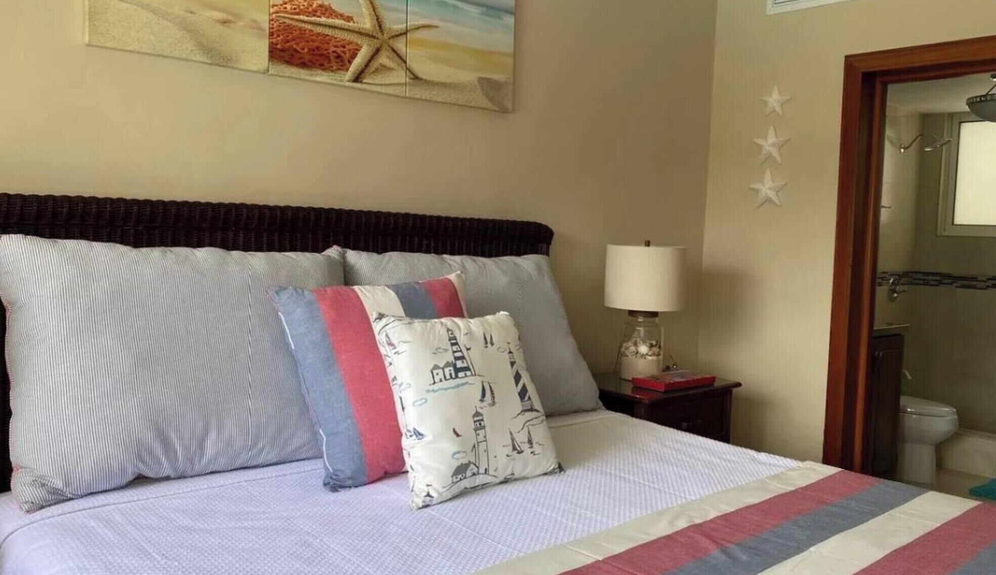 A hotel room with a bed, pillows, a nightstand with a lamp, a painting on the wall, and a door with stars.