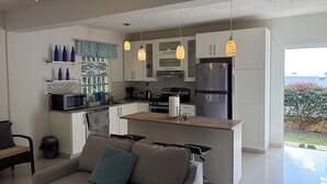 A modern kitchen with white cabinets, a stainless steel refrigerator, and a dining area with a sofa and a coffee table. - Near Beach 2BR Private Backyard, Grill & Laundry (Pelican key)