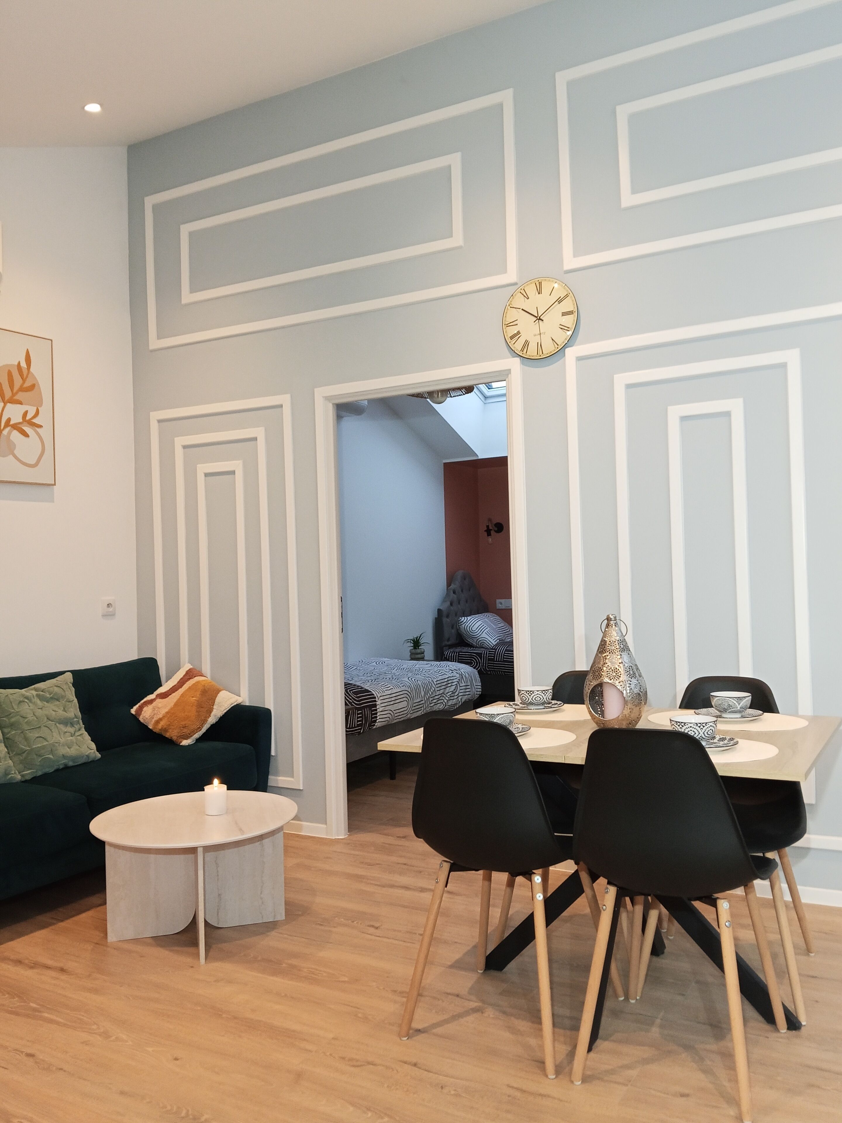A modern living room with a sofa, a coffee table, a dining table with chairs, and a clock on the wall.