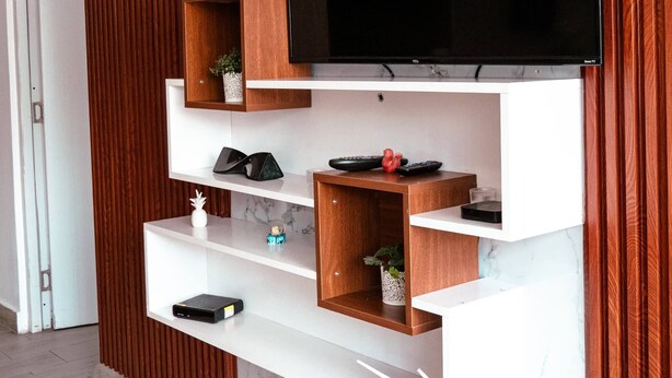 A modern living room with a flat-screen TV mounted on a marble wall, wooden shelves, and a potted plant. - Beautiful, Modern and Central Apartment (Santo Domingo)