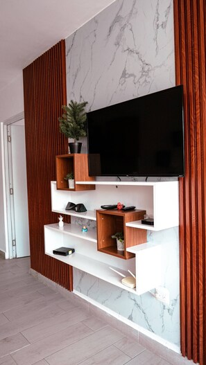 Una sala de estar moderna con un televisor de pantalla plana montado en una pared de mármol, estanterías de madera y una planta en maceta.