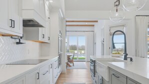A modern kitchen with white cabinets, a large island, and a view to the outdoors. - Modern Luxury Retreat w/ Pool, Spa & Sunset Views (Wallkill)