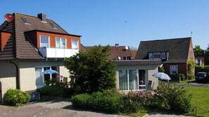 Ein zweistöckiges Haus mit Balkon, Satellitenschüssel und kleinem Garten mit Blumen und Sträuchern.