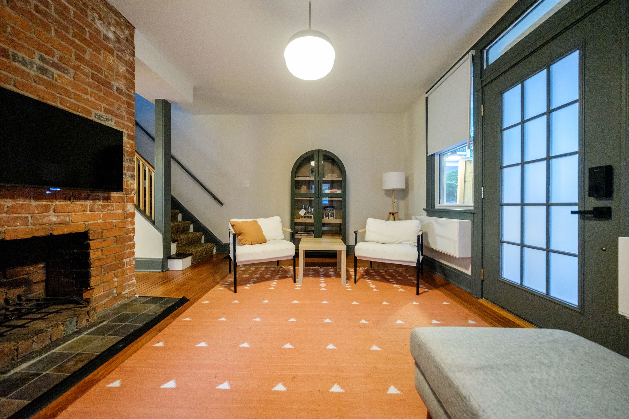 Ein Wohnzimmer mit Kamin, einer Treppe, einem Bücherregal und einem großen Fenster.