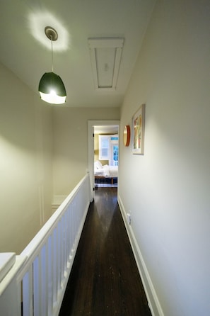 A hallway with a white railing, a ceiling light, and a door leading to a bedroom.
