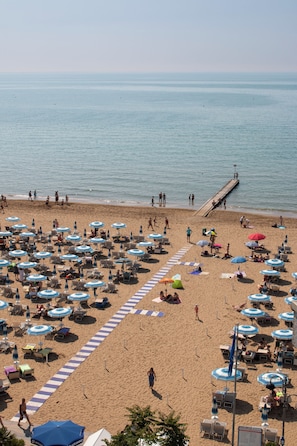 A beach with rows of sun loungers and umbrellas, a pier extending into the water, and a clear view of the sea. - Hotel Rivamare Jesolo (Jesolo)