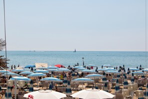 A beach with numerous umbrellas and chairs, a clear sky, and a sailboat in the distance. - Hotel Rivamare Jesolo (Jesolo)