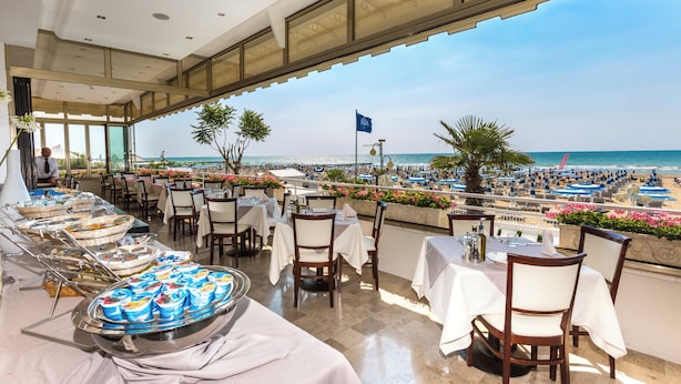 Un espace de restauration aménagé sur le toit, avec des tables et des chaises, un buffet proposant divers plats, et une vue sur la plage.