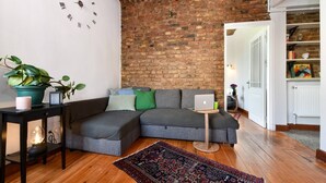 Ein modernes Wohnzimmer mit Ziegelwand, einem Ecksofa, einem kleinen Beistelltisch, einem Laptop und einem dekorativen Teppich.