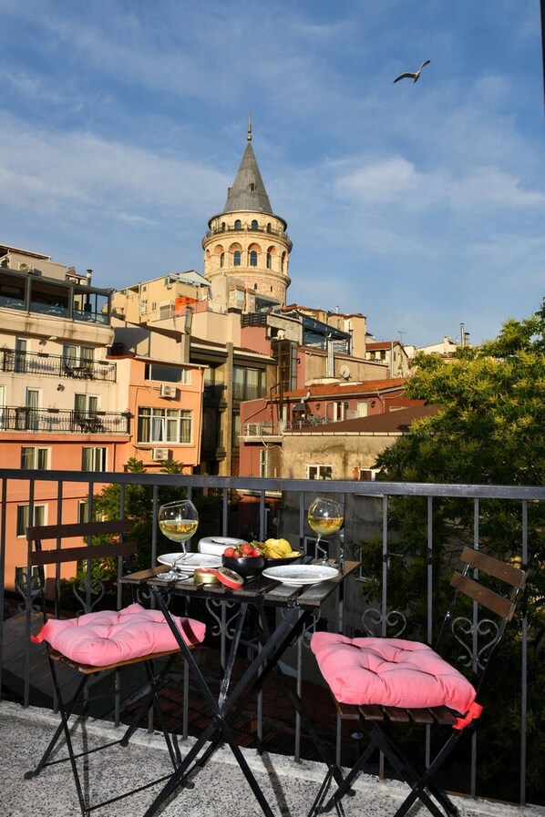 A balcony with a table set for two, overlooking a cityscape with a prominent tower. - Galata Tower at Your Fingertips Private (Istanbul)
