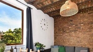 Ein gemütliches Zimmer mit Backstein-Decke, einem Esstisch mit Früchten und Wein, einem grauen Sofa und einem Laptop auf einem kleinen Tisch.